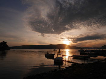 Silhouette boat moored in sea against sky during sunset