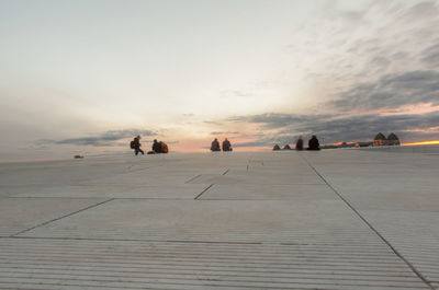 People relaxing on rooftop against sky during sunset