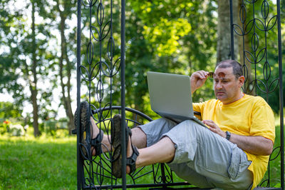 Middle aged man with laptop working outside in garden, green home office concept