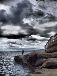 Man standing on sea shore against storm clouds