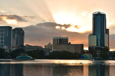 Sea by buildings against sky during sunset