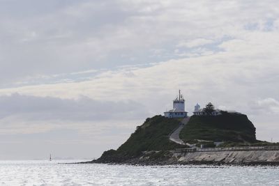 Lighthouse in sea against cloudy sky