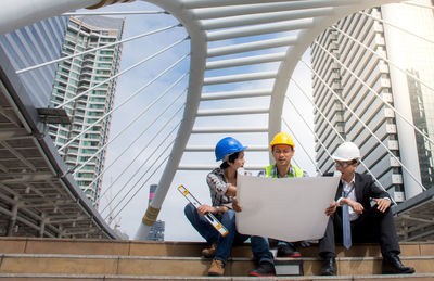 Engineers working over blueprint while sitting in city