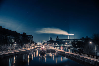 Illuminated city by river against sky at night