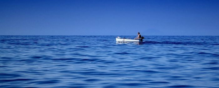 Man sitting in boat on sea against blue sky