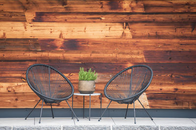 Two metal armchairs and a table with a rosemary stone pot against the background of a wooden wall