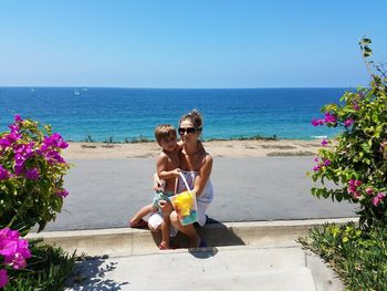 Mother and son on street against sea and sky during sunny day