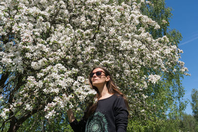 Portrait of beautiful young woman standing by flower tree