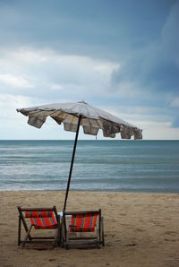 Parasol amidst empty deck chairs on sand at beach against sky