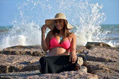 Woman sitting on rock by sea against sky