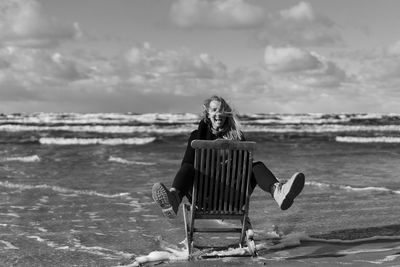 Man sitting on shore at beach against sky