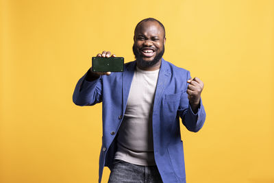 Portrait of young man using mobile phone against yellow background