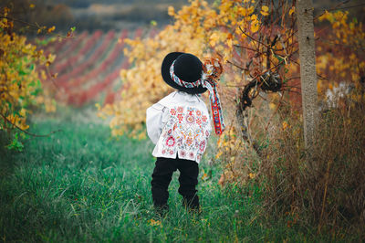 Rear view of person standing by tree on field during autumn