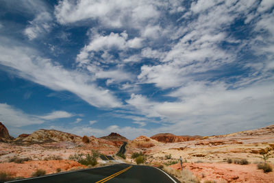 Road amidst land against cloudy sky