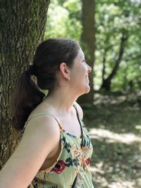Woman looking away while standing on tree trunk in forest