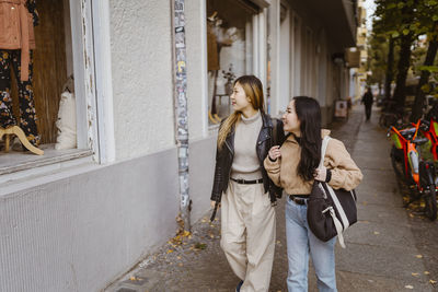 Female friends looking at store window while walking on sidewalk