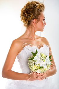 Bride with bouquet looking away while standing against arch