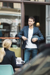 Smiling businessman holding helmet while talking to colleague at sidewalk cafe