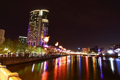 Illuminated city by river against sky at night