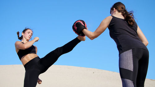 Two athletic, young women in black fitness suits are engaged in a pair work out kicks train to fight