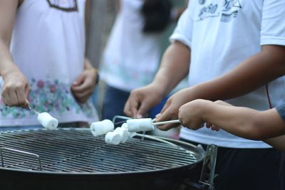 Friends holding marshmallow over barbecue grill
