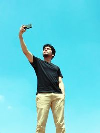 Low angle view of young woman standing against clear blue sky