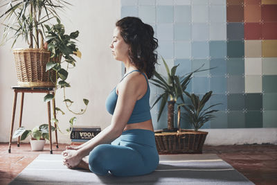 Side view of woman meditating while sitting by potted plants at home