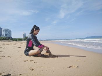 Side view of woman making sandcastle while sitting on beach