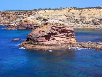 Rock formation in sea against clear blue sky