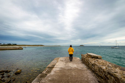 Rear view of mid adult woman standing at beach against cloudy sky