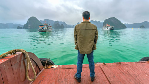 Rear view of man standing on sea against mountains