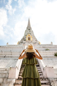 Low angle view of woman standing by building against sky