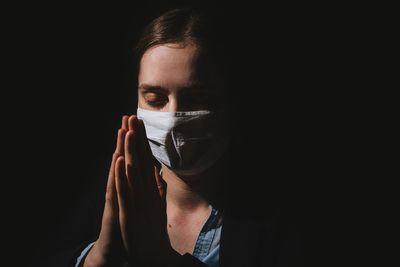 Portrait of woman covering face against black background