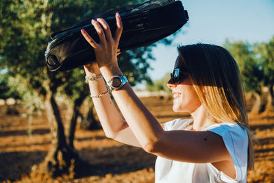 Side view of woman shielding eyes while standing at olive orchard