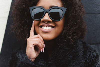 Portrait of woman in sunglasses and fur coat against wall
