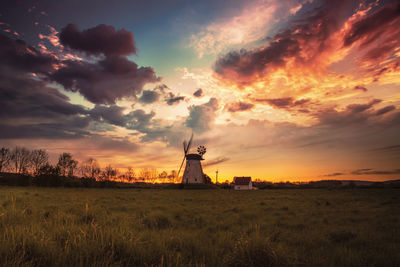 Silhouette traditional windmill on field against sky at sunset