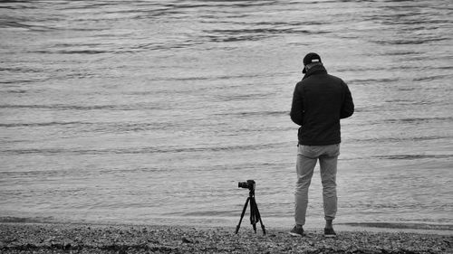 Rear view of man photographing while standing on shore