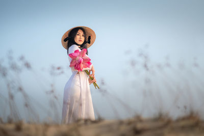 Side view portrait of woman holding flowers while standing on field against sky