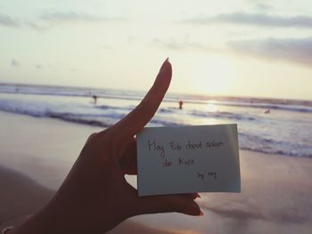 Midsection of hand holding text at beach against sky