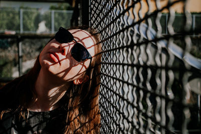 Portrait of young woman standing against chainlink fence