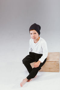 One caucasian cute preschool boy sitting on big box isolated on white studio background, copyspace. 