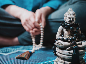 Close-up of buddha figurine against woman with beads sitting on carpet