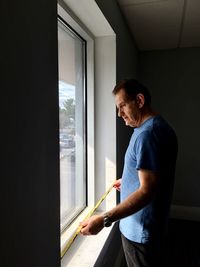 Side view of man measuring window with tape measure at home