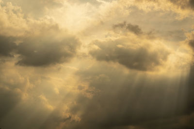 Low angle view of sunlight streaming through clouds