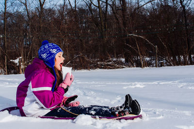 Side view of girl eating snow while sitting outdoors in winter