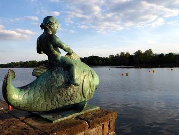 Statue by lake against sky