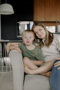 Portrait of mother and son with down syndrome sitting together on sofa at home