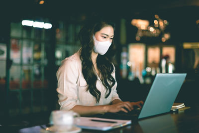 Woman wearing mask using laptop at office