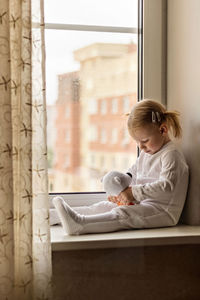 Full length of girl with stuffed toy sitting by window