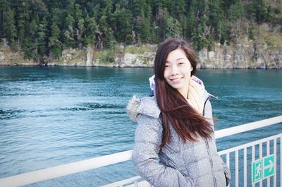 Portrait of smiling woman standing at railing by lake